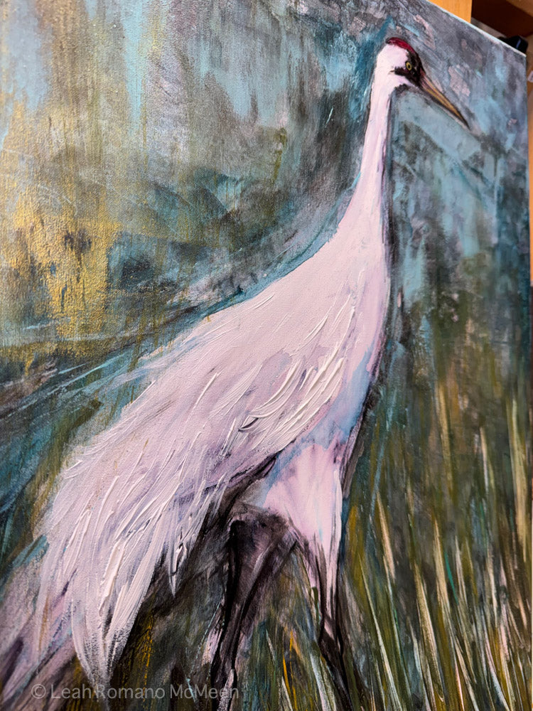 An expressive painting of a white crane standing in a marshy landscape with blue, green, and yellow brushstrokes. The artwork fills the frame, with visible canvas edges and a small artist signature at the lower left.