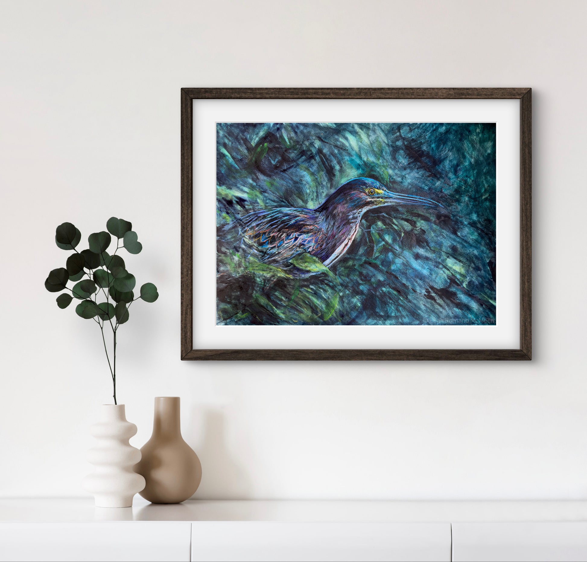 Framed artwork of a bird on water with a vase and plant on a white surface