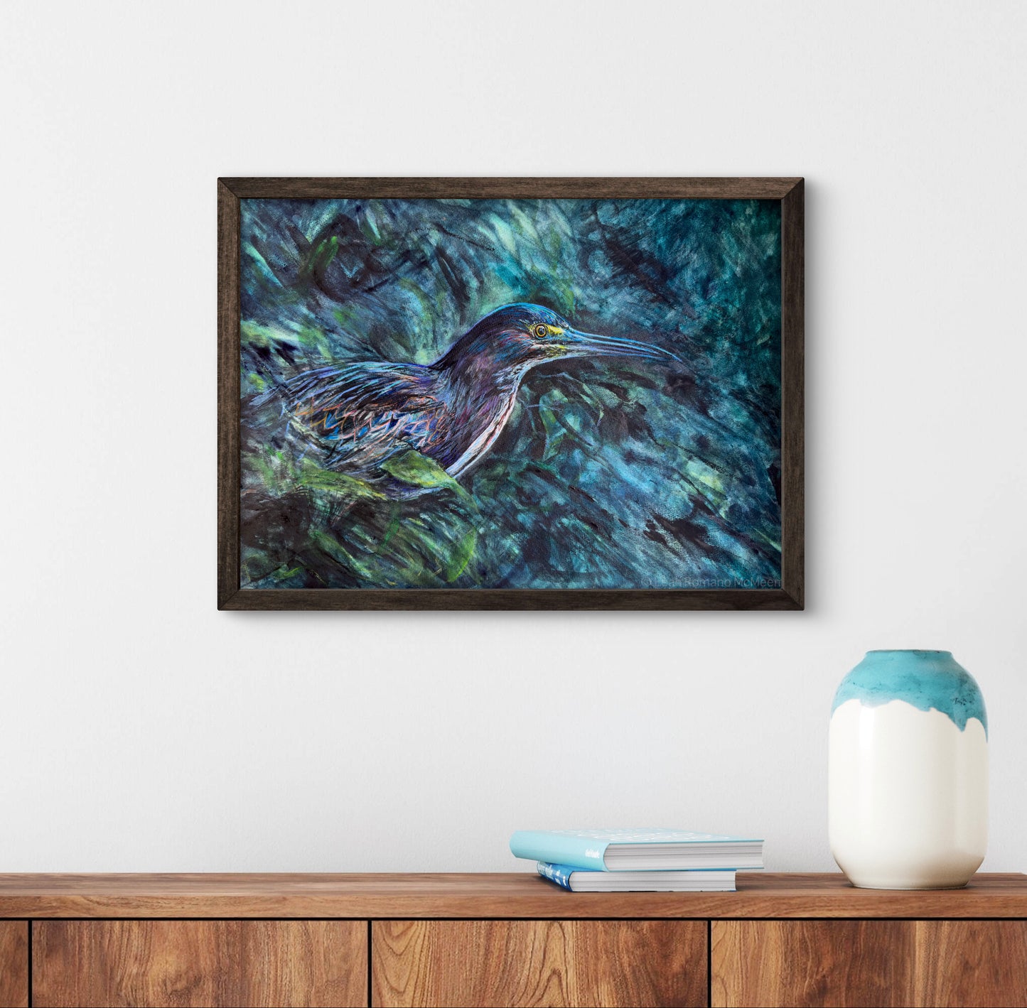 Framed painting of a bird on a wall above a wooden shelf with a vase and books.