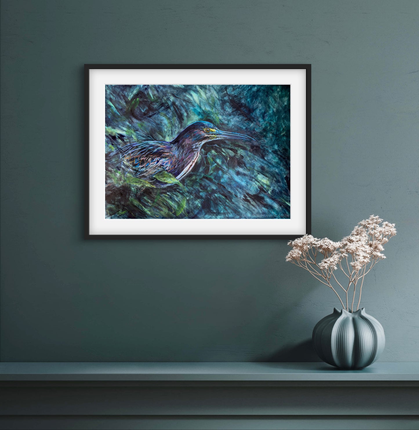 Framed painting of a bird on a dark green wall with a vase of flowers below.