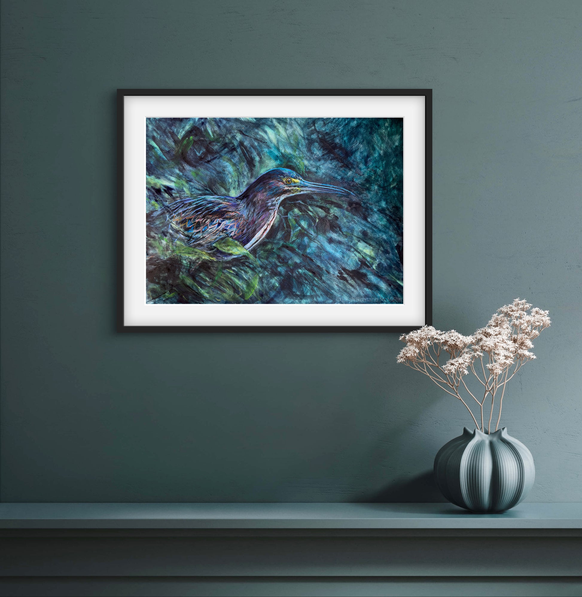 Framed painting of a bird on a dark green wall with a vase of flowers below.