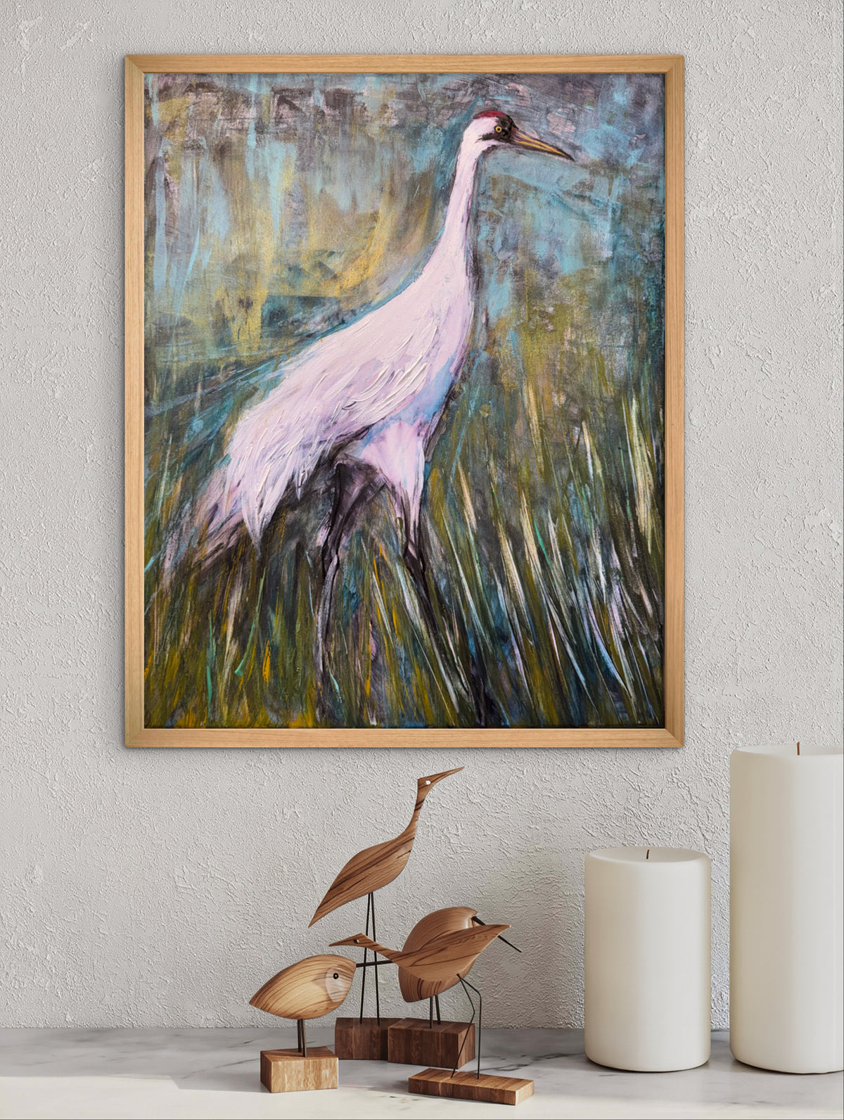 Framed wall art featuring an abstract painting of a white heron in a marsh, displayed on a textured light gray wall above a shelf with wooden bird sculptures and white candles.